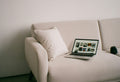 Laptop on a cream sofa with a pillow.